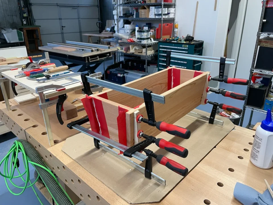 Zusammengespannte Blumenkiste auf einer Werkbank in einer Werkstatt, im Hintergrund Werkzeuge und Materialien.
